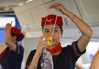 an air stewardess demonstrates how to put on an emergency oxygen mask on a plane, in case of emergency.