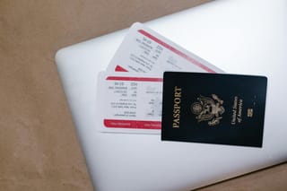 a us passport on top of a laptop with plane tickets underneath the passport.