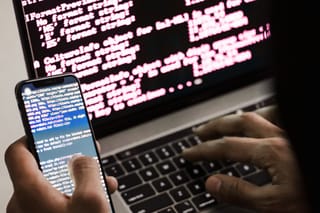an obscured hacker types on a phone terminal while also using a laptop terminal console window