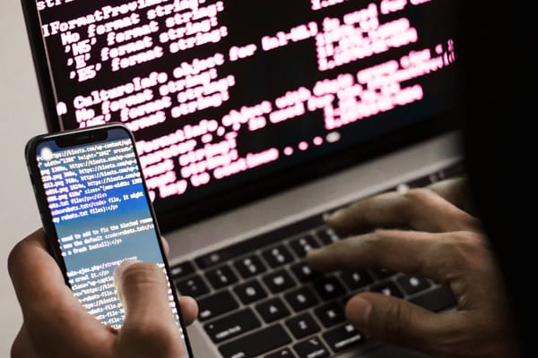 an obscured hacker types on a phone terminal while also using a laptop terminal console window