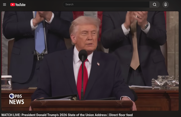 a photo of president trump standing in front of congress wearing a red tie. he is squinting and two men are clapping behind him